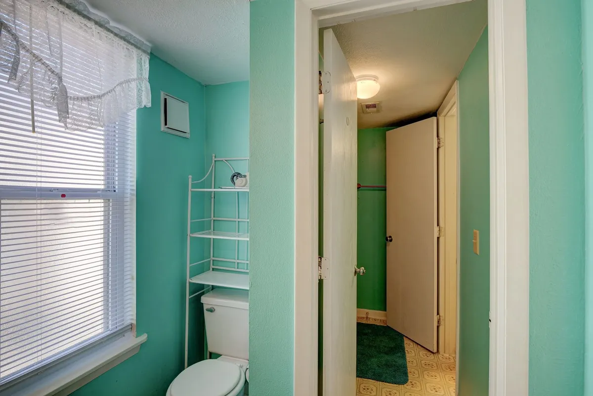 A fresh, well-lit bathroom featuring a toilet, shelving unit, and a window with soft curtains. The bathroom feels clean and functional, providing a private space for personal routines and unwinding after a day of adventure.