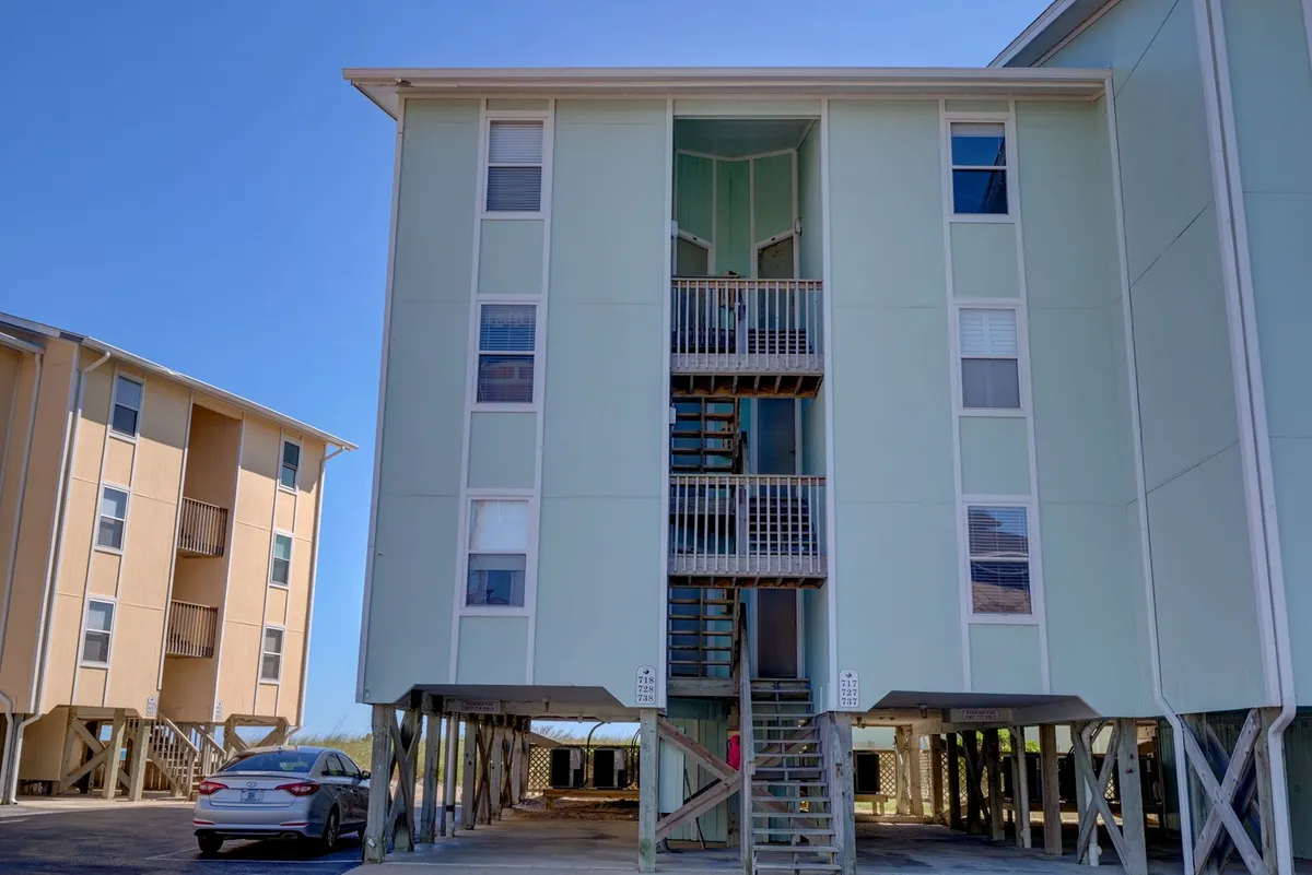 An exterior view featuring a light green building, a prominent staircase, and surrounding structures. The porch and exterior spaces lend themselves to socializing, barbecuing, or simply relaxing in the sun. The environment feels approachable and community-focused, suggesting easy access to outdoor amenities and the beach.