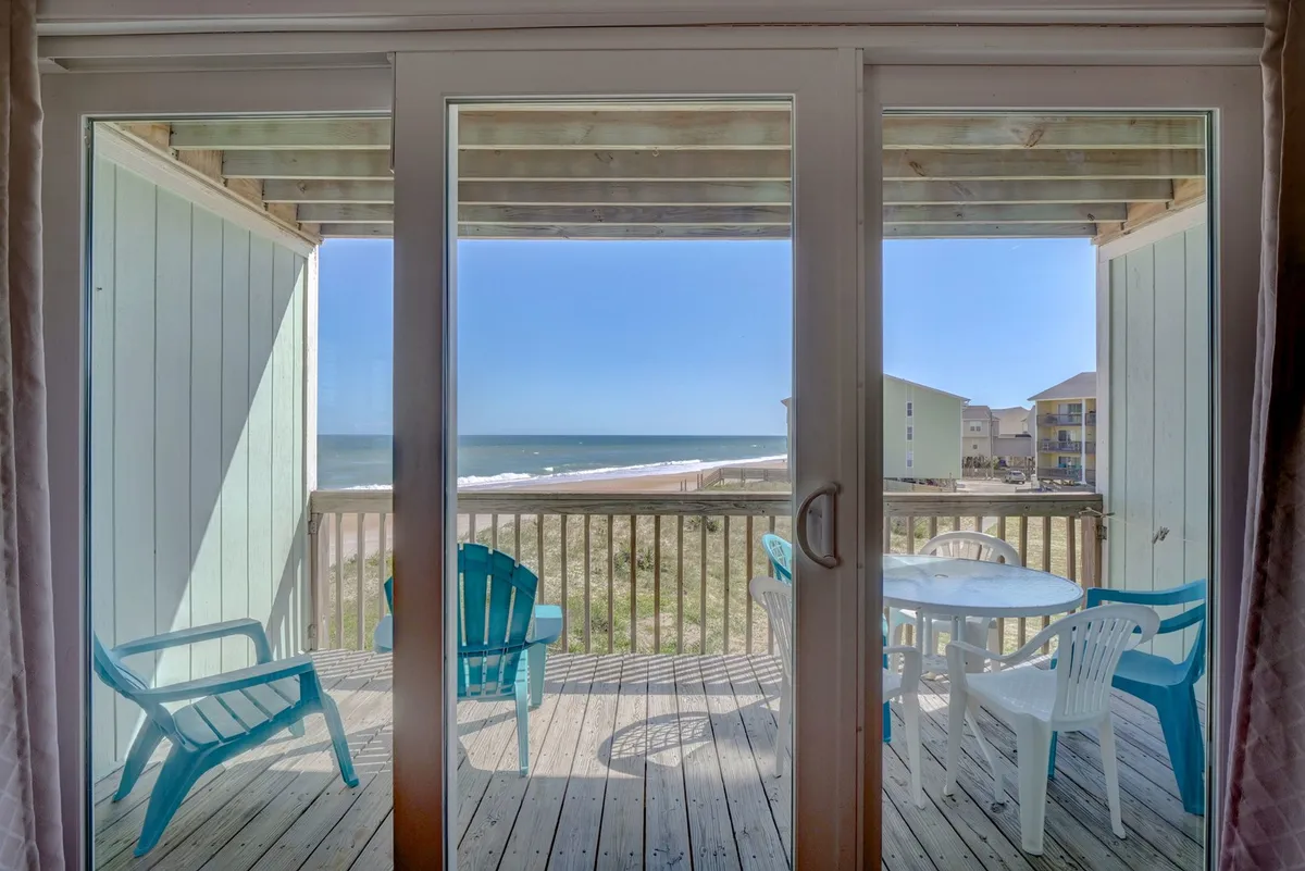 An inviting outdoor seating area with blue chairs and a table, set against a backdrop of the ocean and sandy beach. The vantage point is likely from a deck or patio, with serene views perfect for enjoying the sunrise or relaxing al fresco.