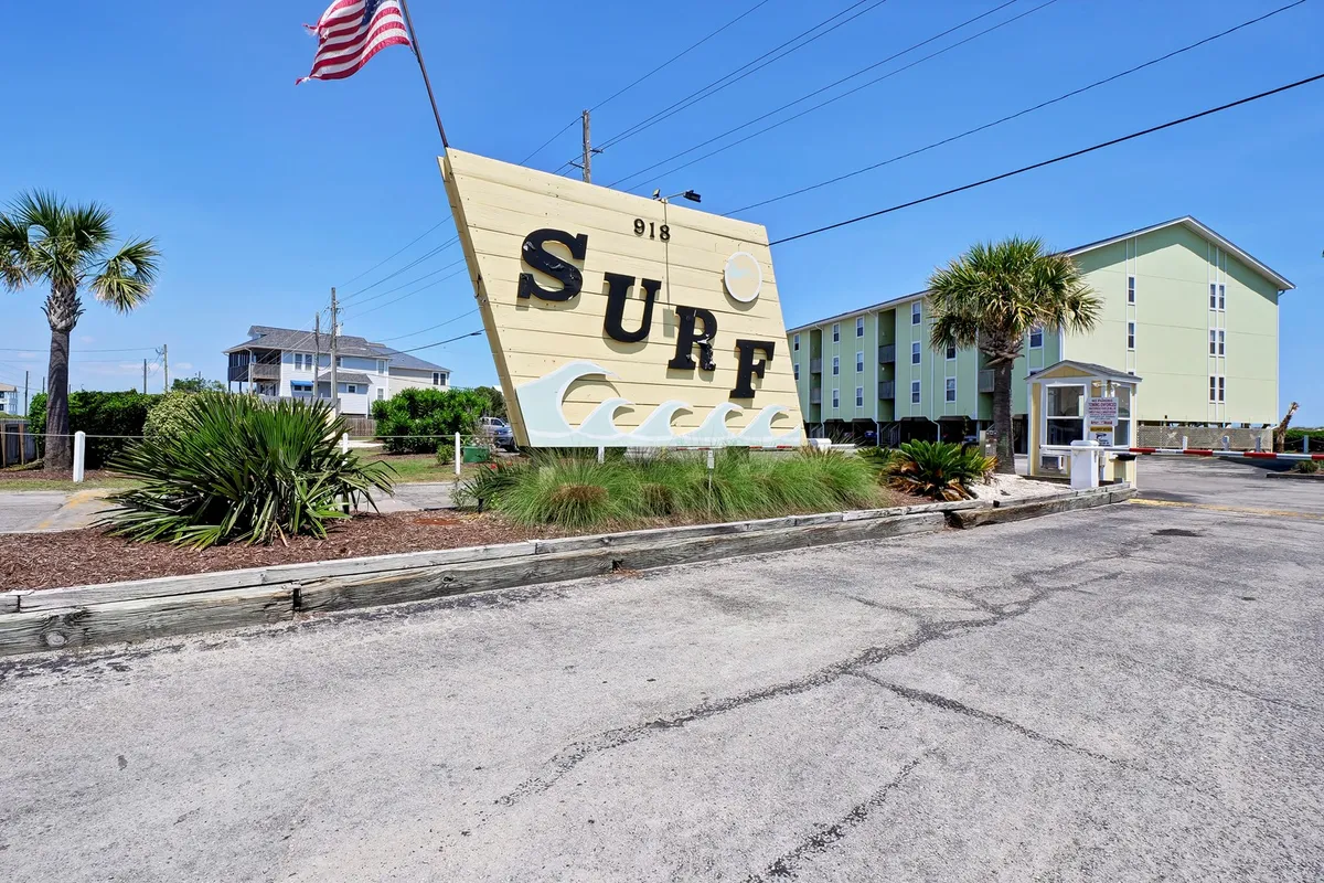 The exterior of Surf Condos, marked by a large 'SURF' sign and surrounded by palm trees. The building facade is lively and welcoming, hinting at the resort-style amenities like the pool and easy access to the beach, while providing a sense of arrival and location.