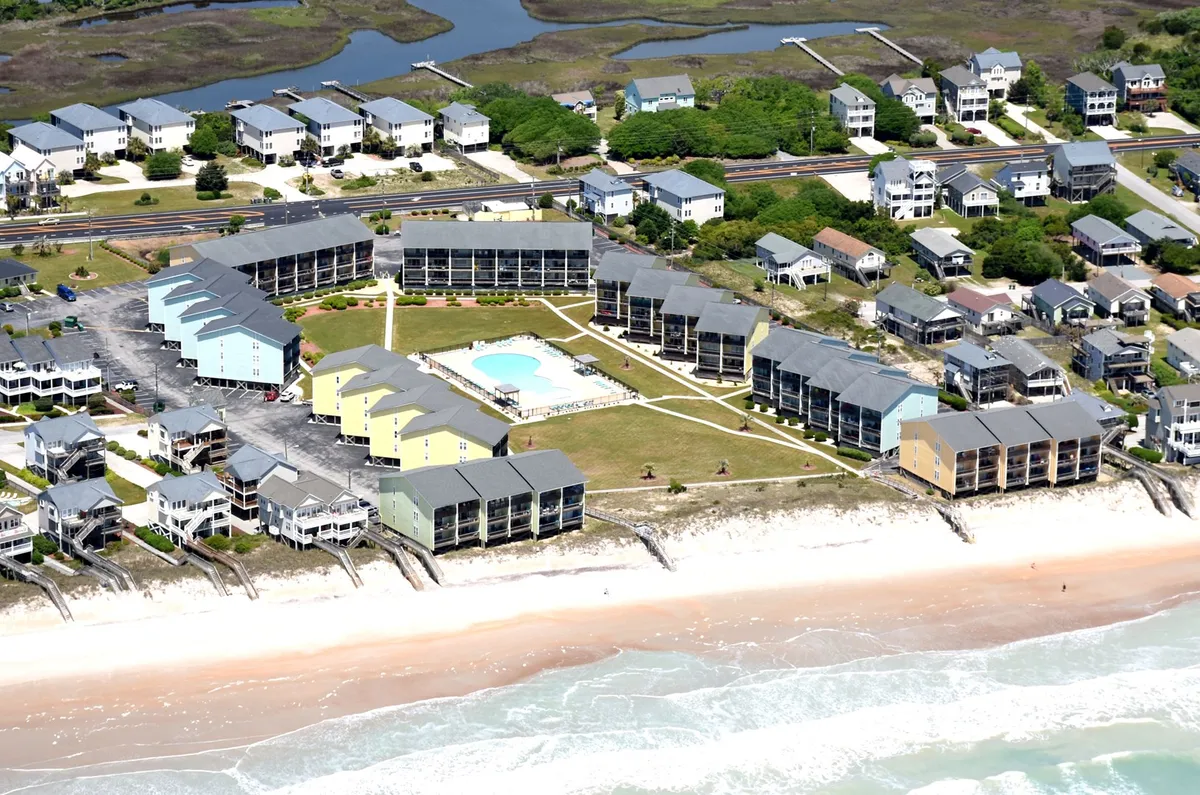 A vibrant scene showing beachfront properties with lush landscaping, a large swimming pool, and the ocean beyond. The pool area is inviting, with space for family gatherings. The image links the residential experience directly to both the pool and the beach, giving a sense of proximity and resort-style amenities.