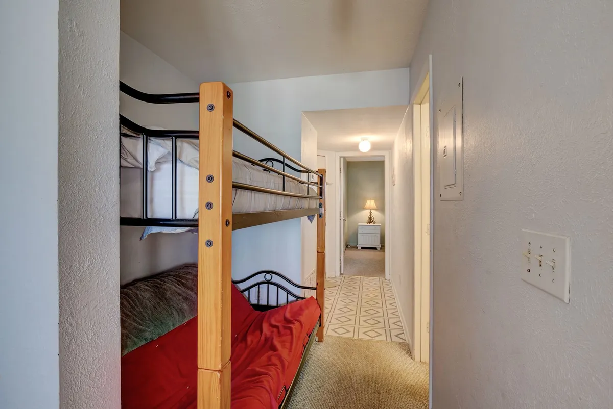 A playful and functional bunk alcove with built-in twin bunks and bright red bedding. The design is compact yet comfortable, with a hallway leading to other rooms, hinting at the convenience and accessibility for kids or friends. The mood is lively yet restful, ideal for younger guests or additional travelers.