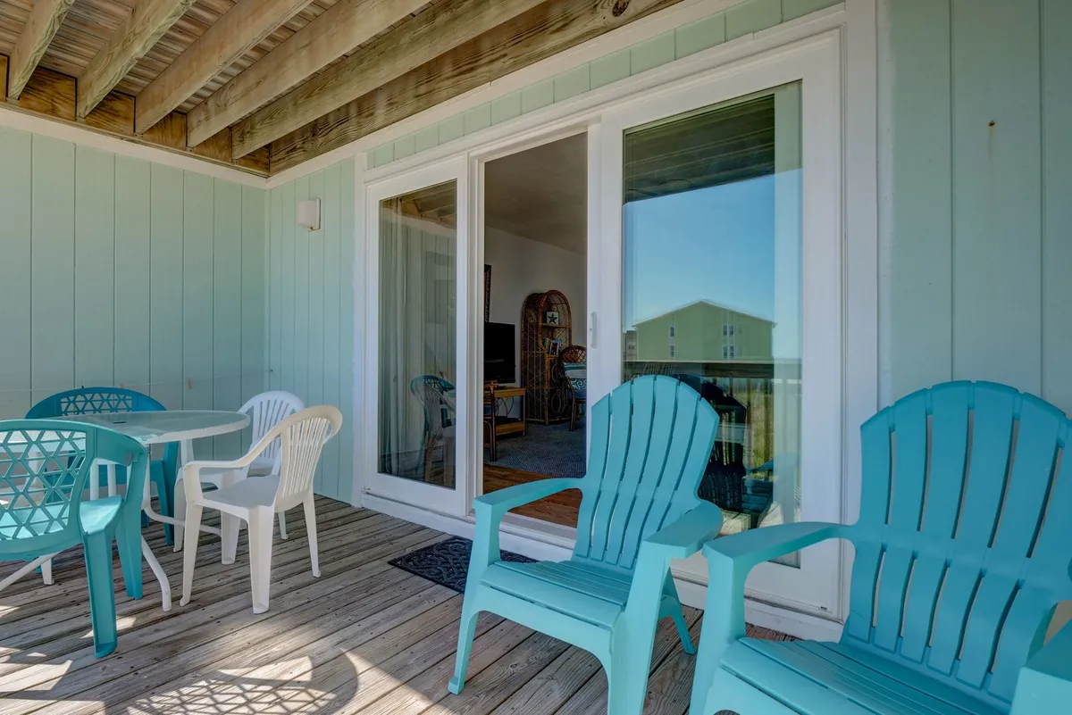 An inviting exterior seating area featuring turquoise chairs, a white table, and a sliding glass door. The tranquil mood suggests a perfect spot for morning coffee, reading, or casual outdoor meals, reinforcing the relaxing, affordable vacation atmosphere.