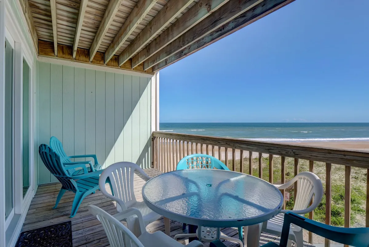 An inviting private deck overlooks the ocean, complete with comfortable outdoor seating and a glass table. The tranquil setting is perfect for morning coffee, sunbathing, or enjoying sunset drinks while listening to the sound of the waves.