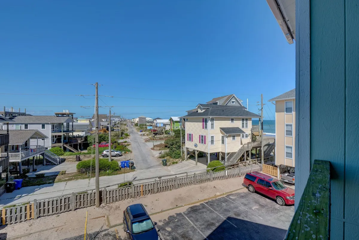 A picturesque street view featuring classic beach houses, a paved road, and the distant ocean. The scene suggests leisurely strolls, easy access to local shops and restaurants, and the relaxed vibe of Surf City.